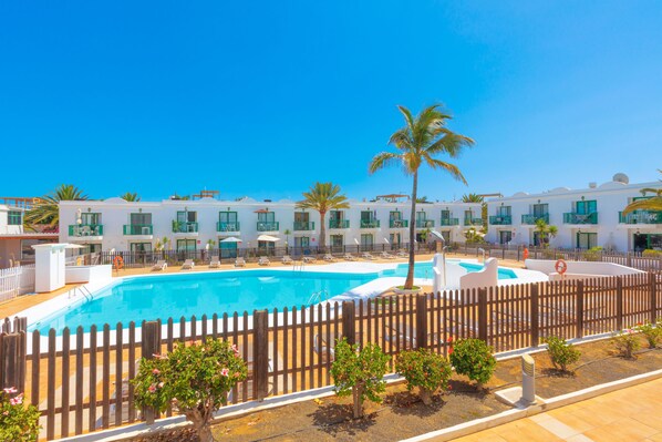 A hotel with a swimming pool, multiple balconies, and a wooden fence.