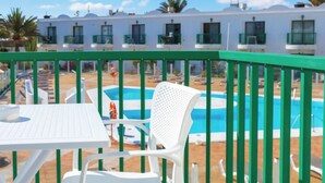 Un espace aménagé au bord de la piscine, avec une table et des chaises blanches, une piscine, et un bâtiment avec de nombreuses fenêtres en arrière-plan.