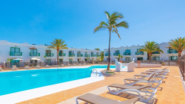 Un espace aménagé au bord de la piscine, avec des chaises longues, une piscine et une rangée de bâtiments d’hôtel dotés de balcons.