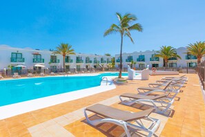 Zona junto a la piscina con sillones de descanso, una piscina y una fila de edificios de hotel con balcones.