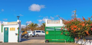 A gated parking area with vehicles, a green wall with a white gate, and a clear blue sky.
