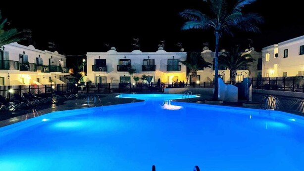 Ein Schwimmbecken bei Nacht mit freiem Blick auf die umliegenden Gebäude und Palmen.