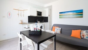 A modern kitchen with a microwave, coffee machine, and washing machine. There is a dining table with chairs and a gray sofa with colorful cushions. - Desert Pool View & WiFi by iRent Fuerteventura (Corralejo Playa)