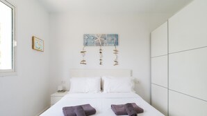 A neatly made bed with two folded towels, a white headboard, and a wall-mounted artwork depicting fish and sea elements. - Desert Pool View & WiFi by iRent Fuerteventura (Corralejo Playa)