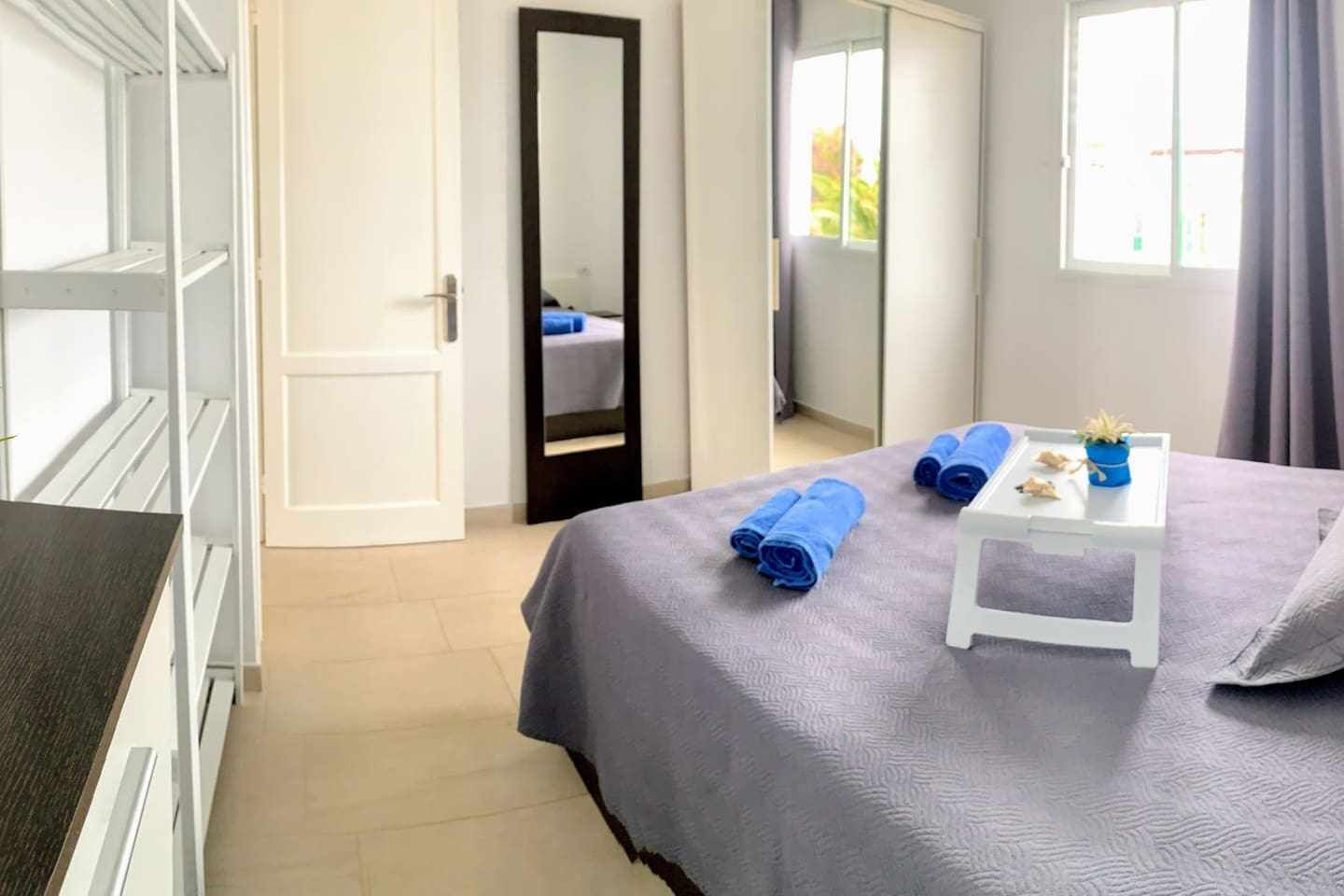 A bedroom with a bed, a bedside table with towels, a mirror, and a wardrobe.
