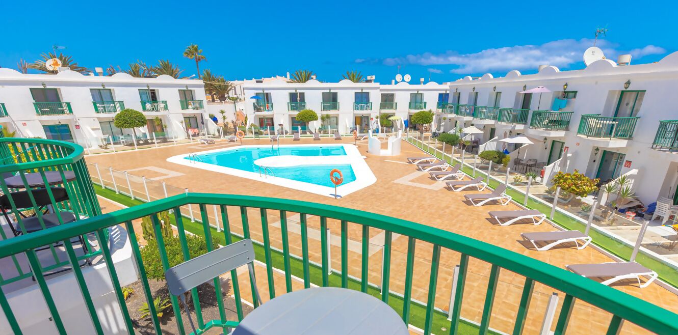Un hotel con piscina, tumbonas y barandilla verde.