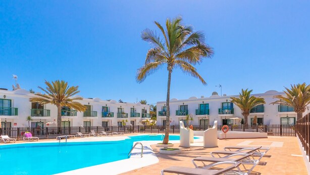 Un espace piscine d’hôtel avec de nombreux chaises longues, des palmiers et un ciel d’un bleu limpide.