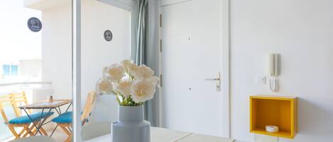 Une chambre d’hôtel moderne avec une table à manger, un vase de fleurs, une étagère jaune et une vue sur le balcon extérieur.