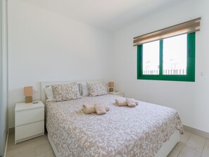A bedroom with a bed, two bedside tables, a window, and a view of the outside. - Sea Breeze Pool View & WiFi by iRent Fuerteventura (Corralejo)