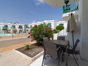 A patio with a table and chairs, a small garden, and a pool in the background. - Sea Breeze Pool View & WiFi by iRent Fuerteventura (Corralejo)
