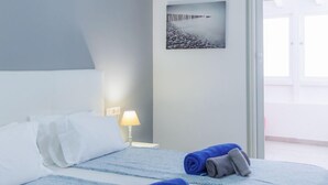 Quarto de hotel com cama, mesa de cabeceira com abajur, um quadro na parede e vista para o exterior.