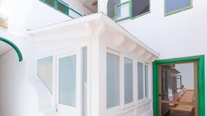 Um edifício branco com um alpendre coberto, um vaso de planta e uma escadaria de madeira que leva a um andar superior.