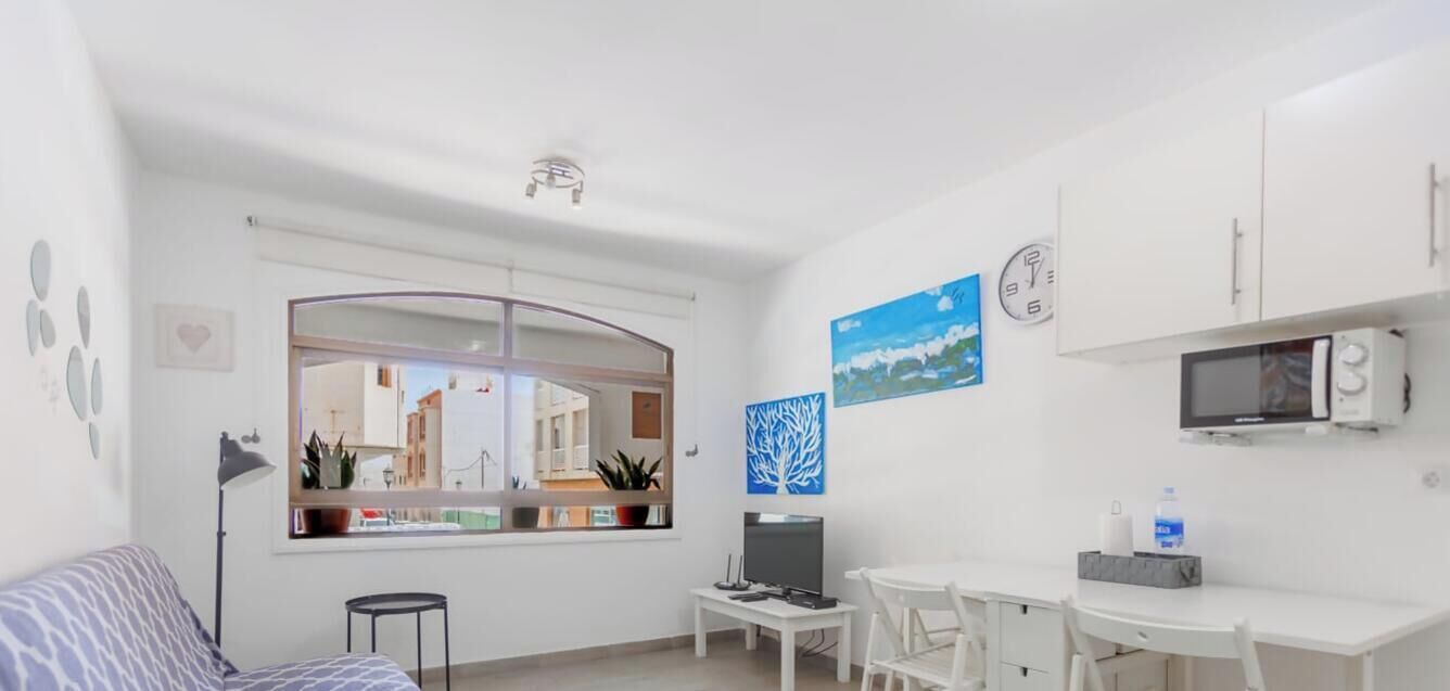 A compact living space with a sofa, a small table, a TV, and a window with a view of buildings.