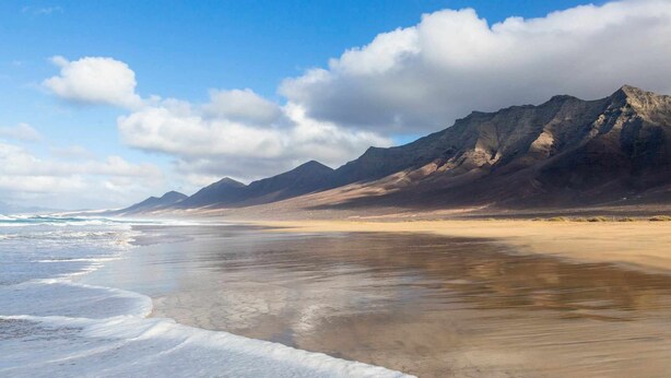 Uma praia com uma cadeia de montanhas ao fundo.