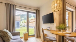 Una sala moderna con sofá, una mesa de comedor con sillas, un televisor montado en la pared y un amplio ventanal con cortinas.