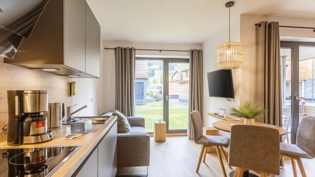 Una cocina moderna con cafetera, zona de comedor con mesa y sillas, y un televisor montado en la pared.