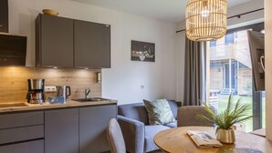 Cocina moderna con armarios grises, una cafetera y una encimera de madera. Hay un sofá gris con una planta sobre la mesa auxiliar.