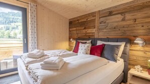 Un dormitorio con una cama grande, paredes de madera, una ventana con vistas a un bosque y una mesita de noche con una lámpara.