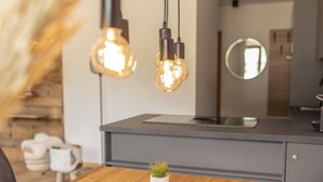 Una cocina moderna con una mesa de comedor de madera, dos plantas en macetas e iluminación colgante.