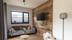 Una sala moderna con un sofá gris, una mesa de centro redonda de madera, un perro blanco y marrón esponjoso, y una lámpara de pie negra.
