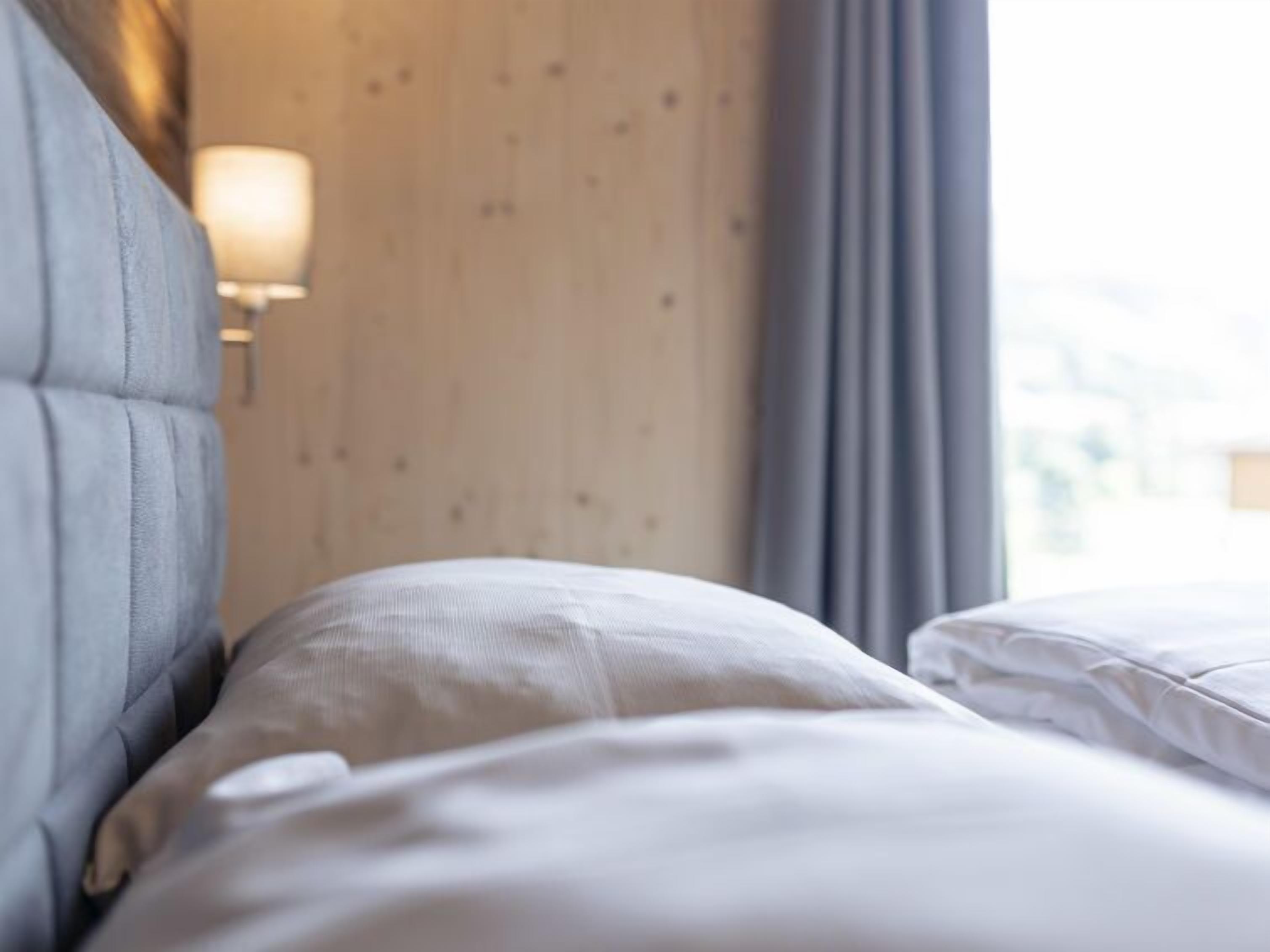 Ett hotellrum med en sänggavel i trä, en sänglampa och utsikt över omgivningarna genom ett fönster.