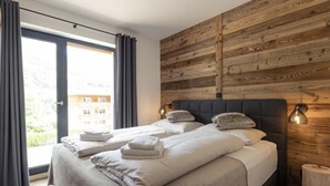 A modern bedroom with two beds, wooden paneling on the wall, and a view of buildings outside. - Superior mit 3 Schlafzimmern & IR-Sauna by Interhome (Sankt Georgen am Kreischberg)