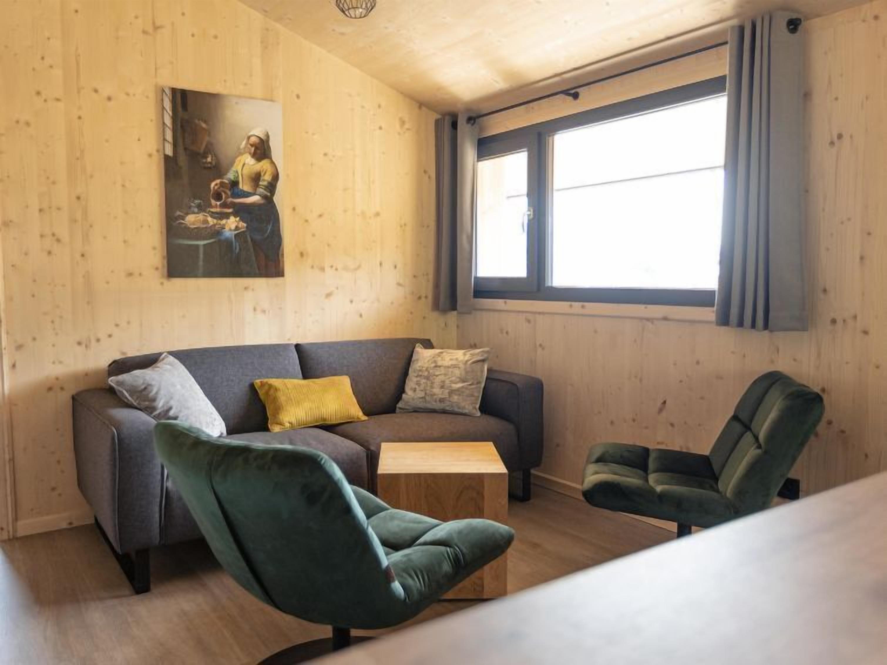 A cozy living room with a grey sofa, two green armchairs, a wooden coffee table, and a painting on the wall.
