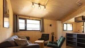 A cozy wooden interior with a sofa, a green armchair, a small table, and a kitchen area with a TV. - Superior mit 3 Schlafzimmern & IR-Sauna by Interhome (Sankt Georgen am Kreischberg)