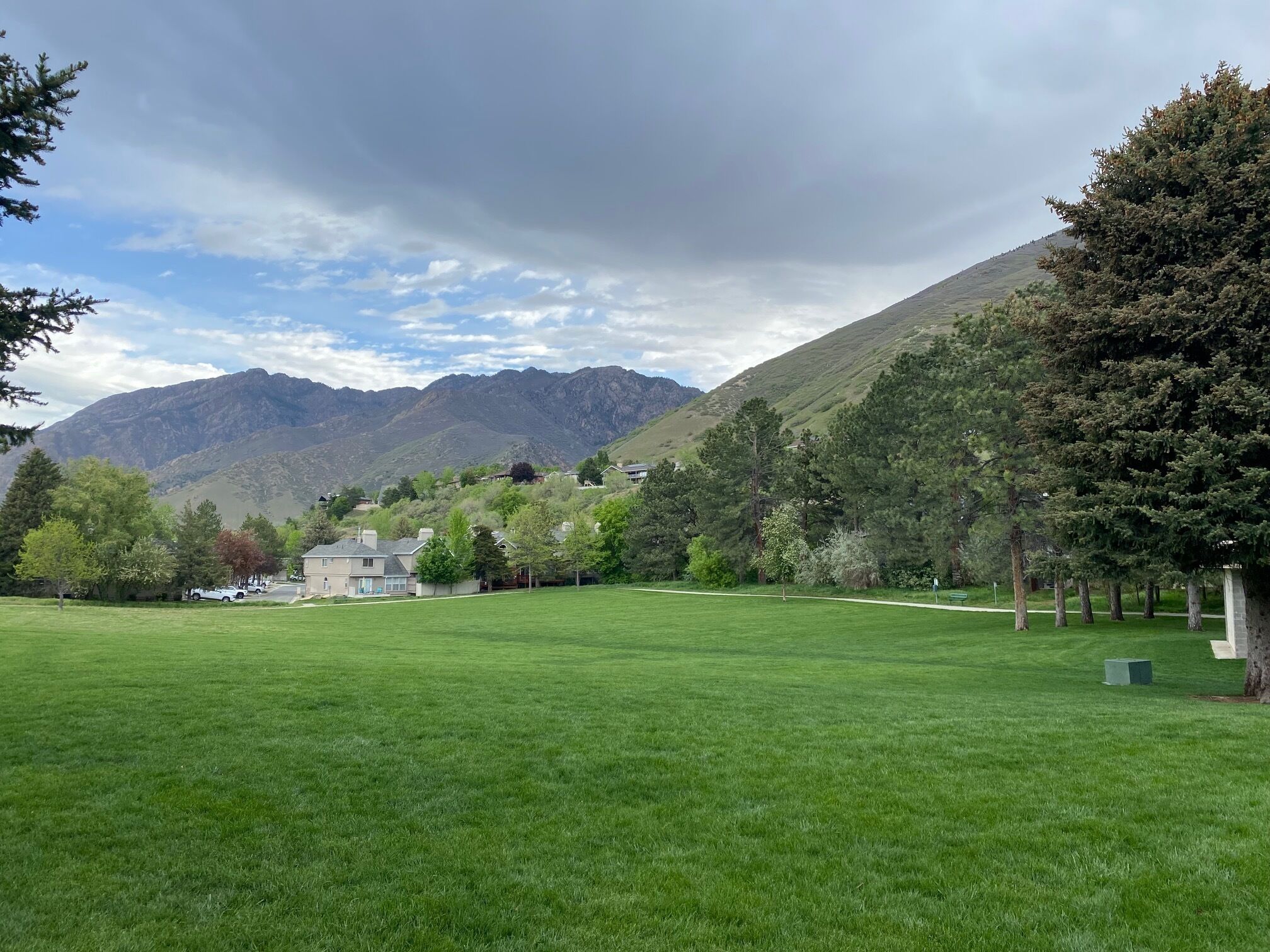 A grassy field with a house and mountains in the background.