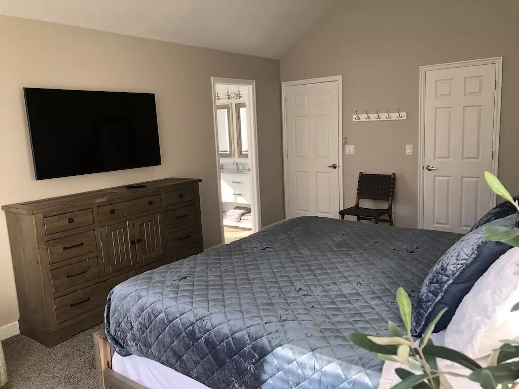 A bedroom with a large bed, a dresser, a television, and two doors.