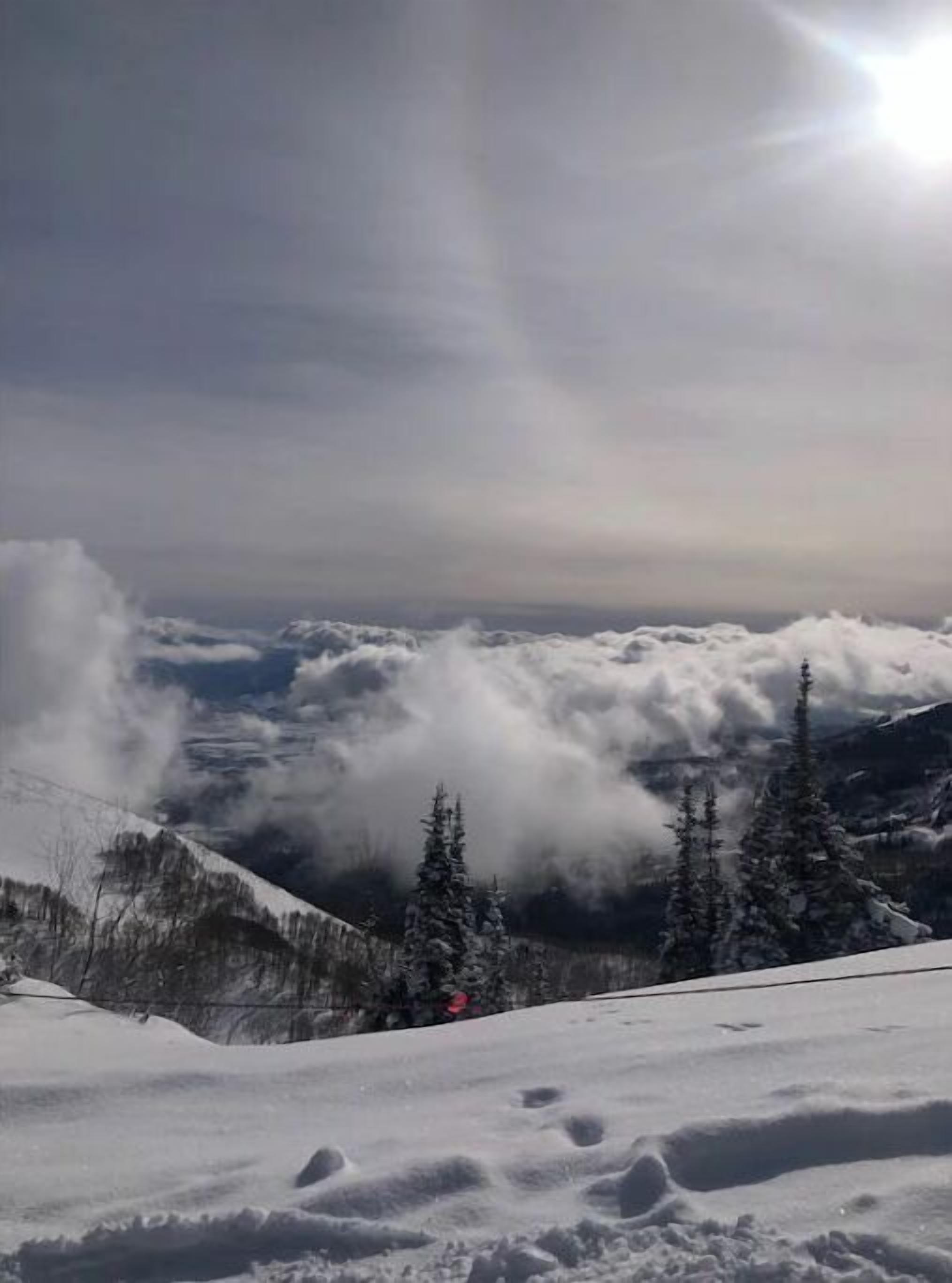 Un paisaje montañoso nevado, cielo despejado y el sol brillando desde la derecha.