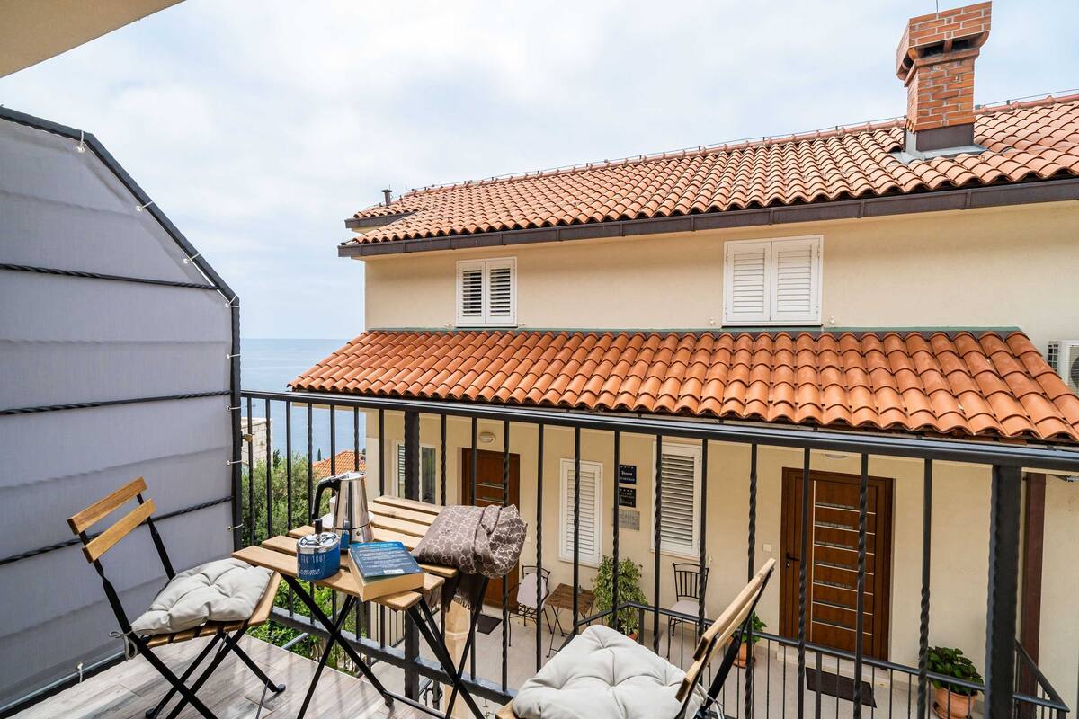 A balcony with a table, chairs, and a view of a building with a tiled roof.