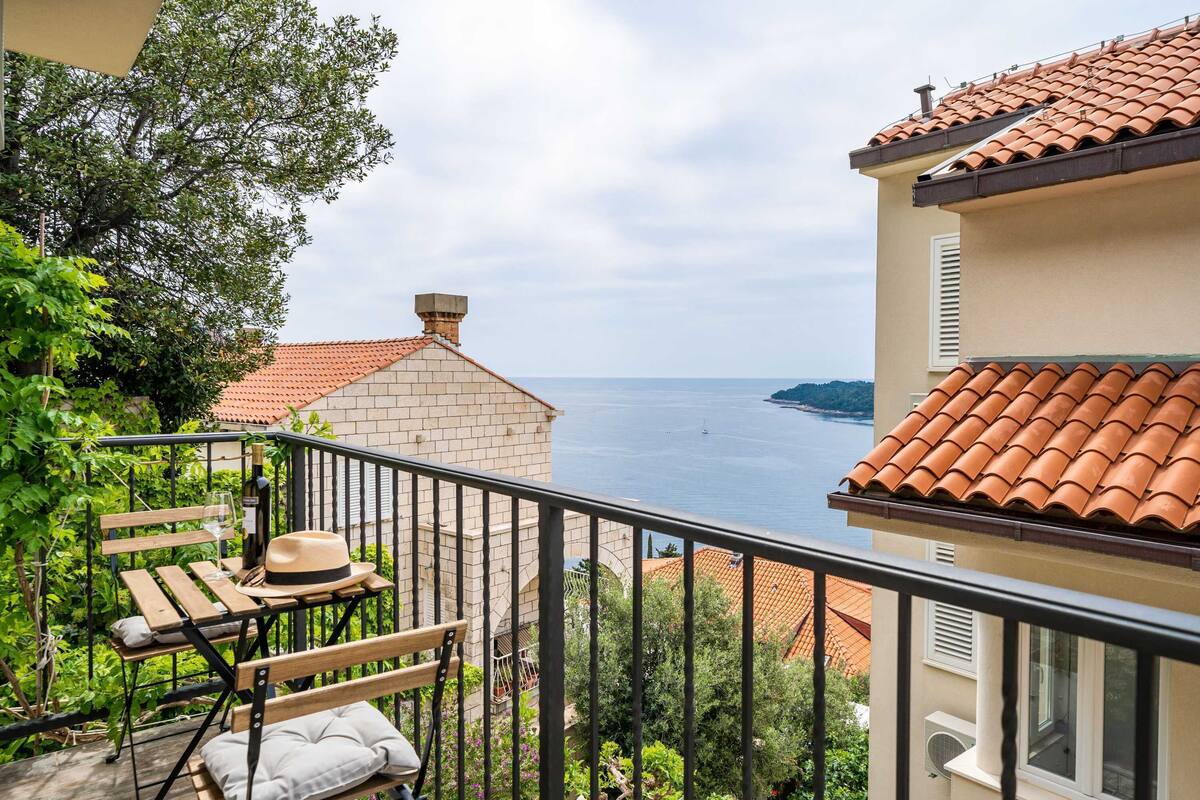 A balcony with a view of the sea, a wooden bench, and a hat.