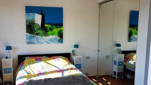 Une chambre à coucher avec un lit, deux tables de chevet, un miroir et un tableau accroché au mur.