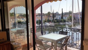 Un balcon avec une table et des chaises, donnant sur une marina où l’on peut admirer des bateaux et des bâtiments.