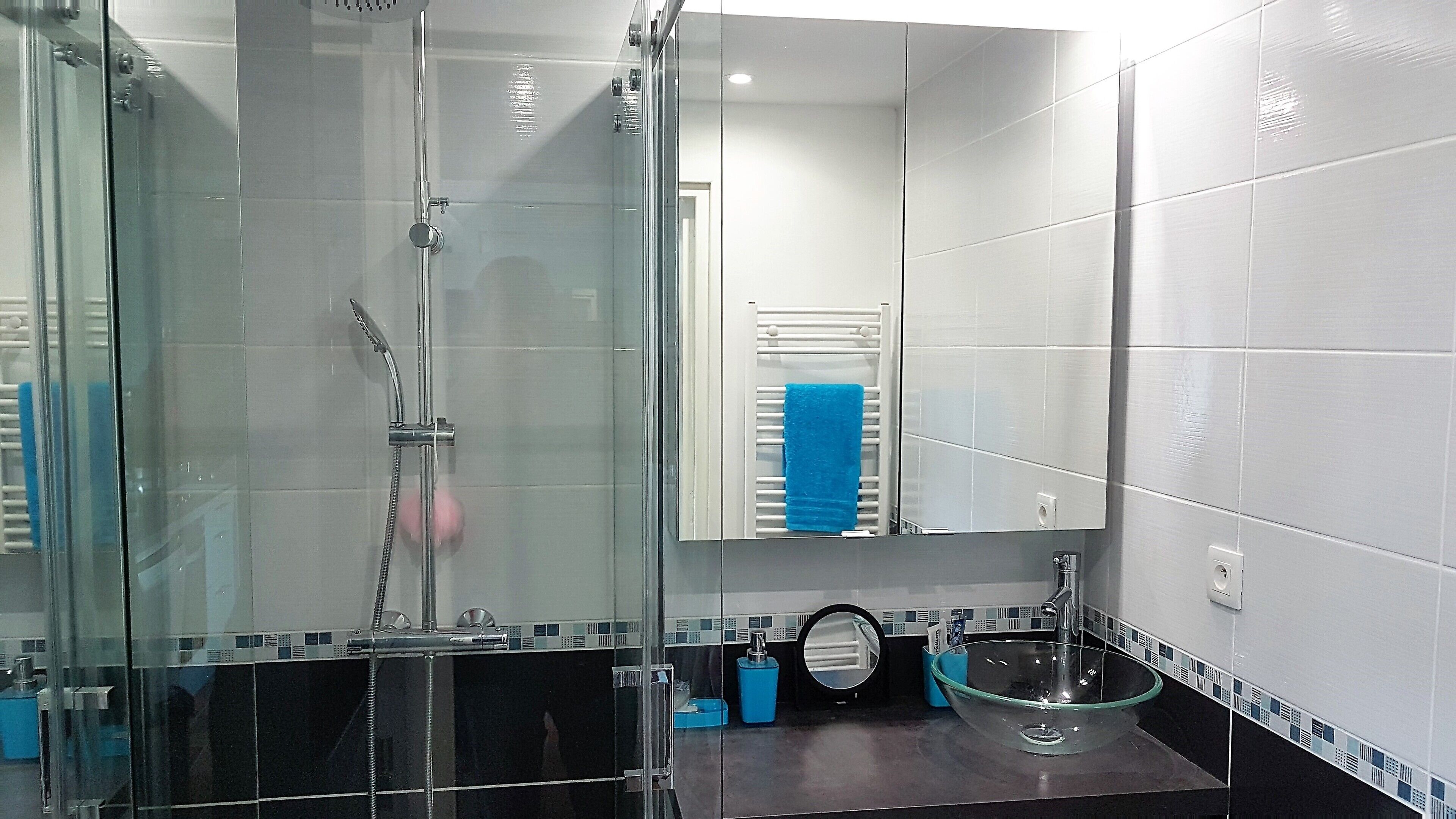 A modern bathroom with a glass-enclosed shower, a sink with a glass basin, and a mirror above the sink.