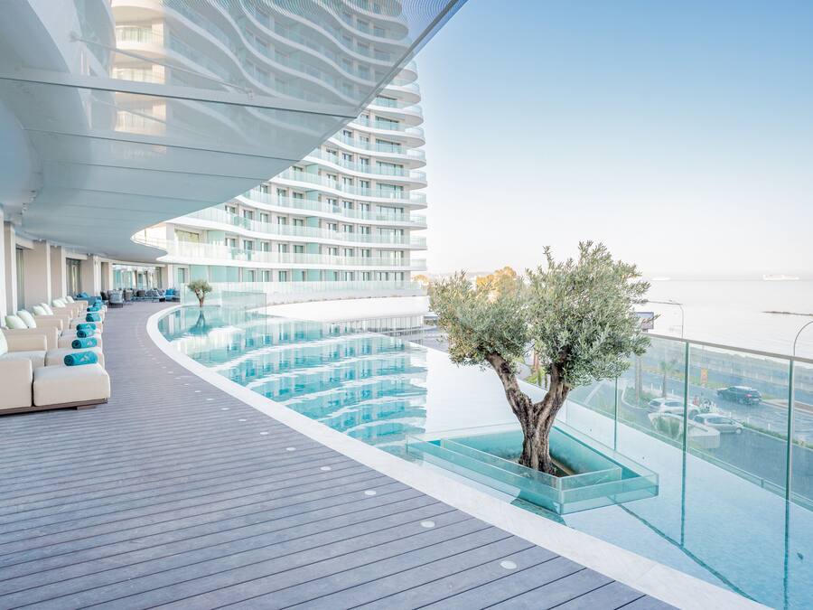 A modern cruise ship deck with a glass infinity pool, outdoor seating, and a view of the ocean.