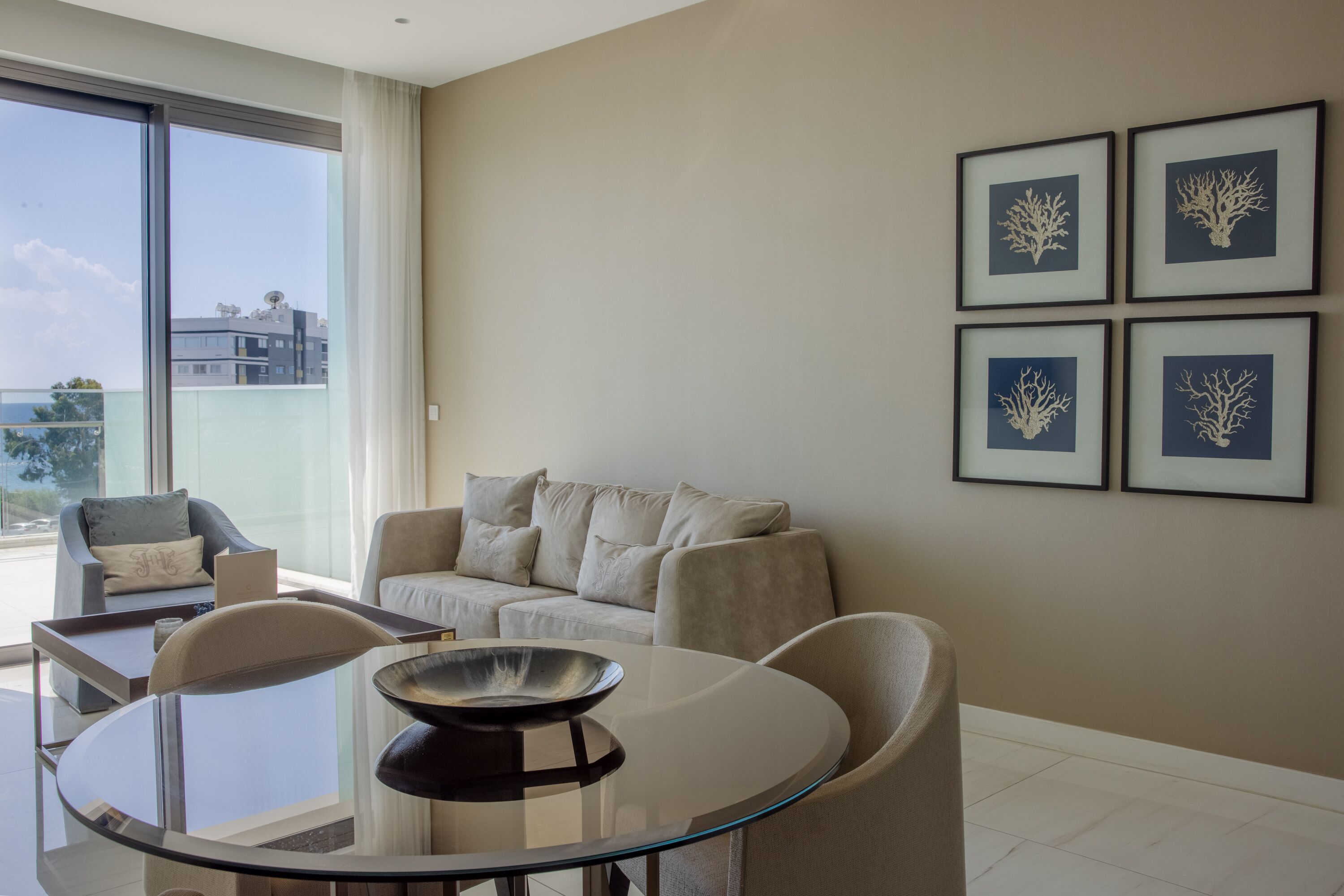 A modern living room with a glass table, two sofas, and framed artwork on the wall.