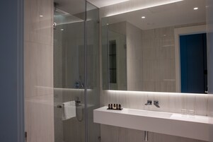Un baño moderno con cabina de ducha de vidrio, un lavabo blanco con dos grifos y un espejo sobre el lavabo.