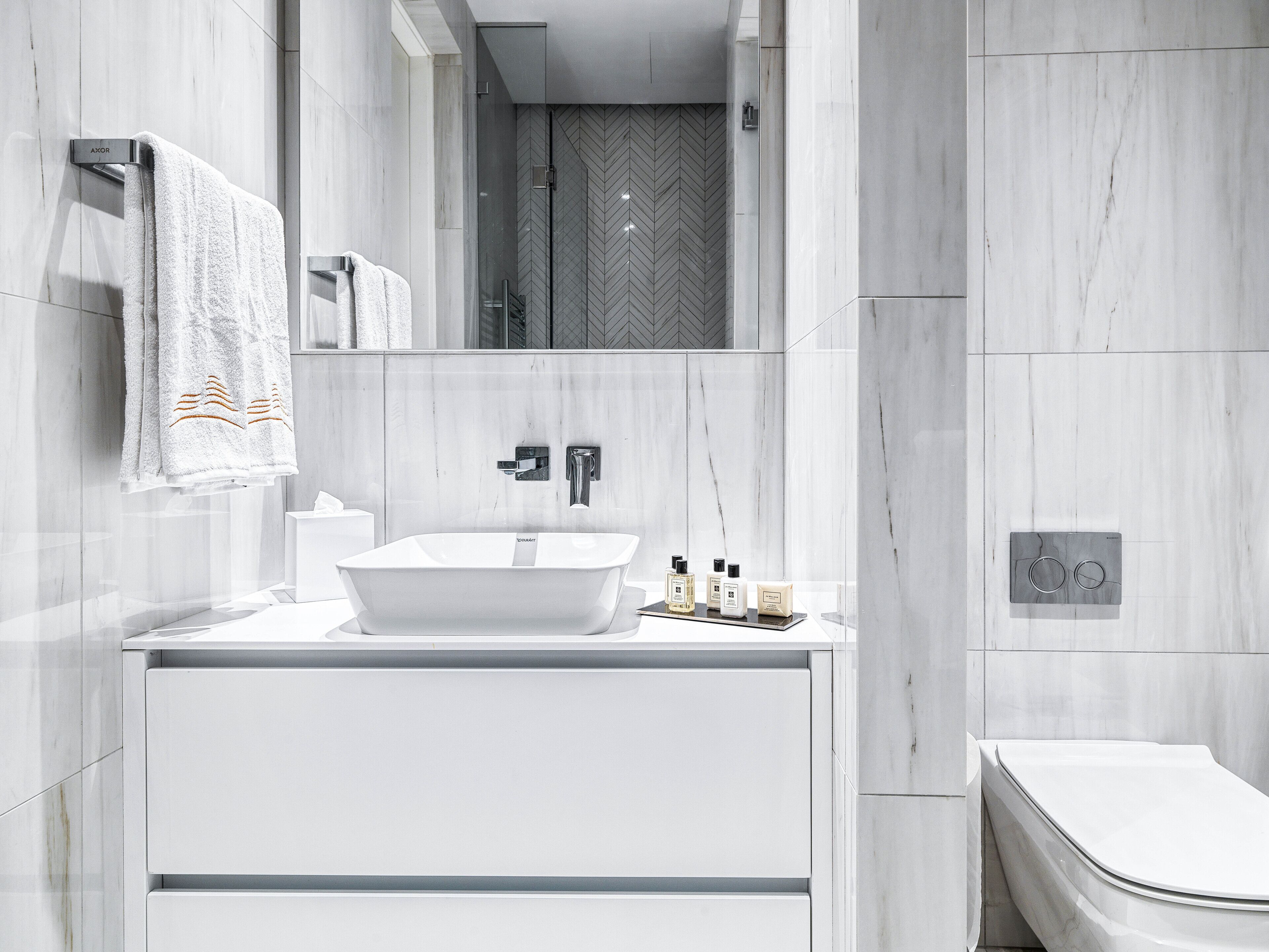 Un baño moderno con tocador blanco, un espejo grande y una bañera independiente.