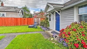 A residential backyard with a wooden fence, a blue door, and a variety of flowering plants. - Lovely Tacoma Cottage w/ Fire Pit, Near Dtwn! (Tacoma)