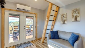 A room with a gray sofa, a wooden ladder, and a view through glass doors to an outdoor deck. - Pet-Friendly Studio w/ Hot Tub & Views in Marshall (Marshall)