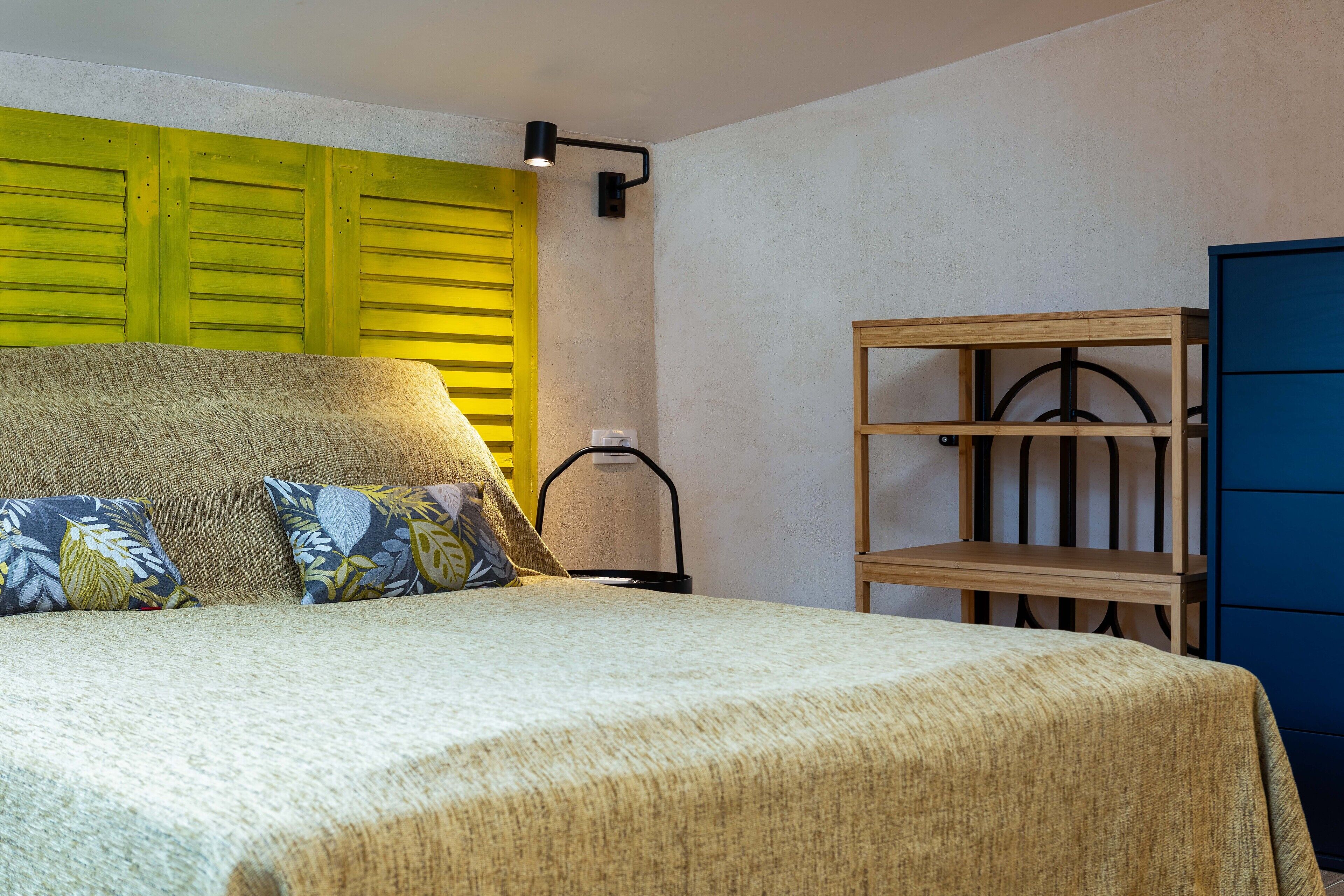 Un dormitorio con una cama, almohadas, un estante de madera y un armario azul.