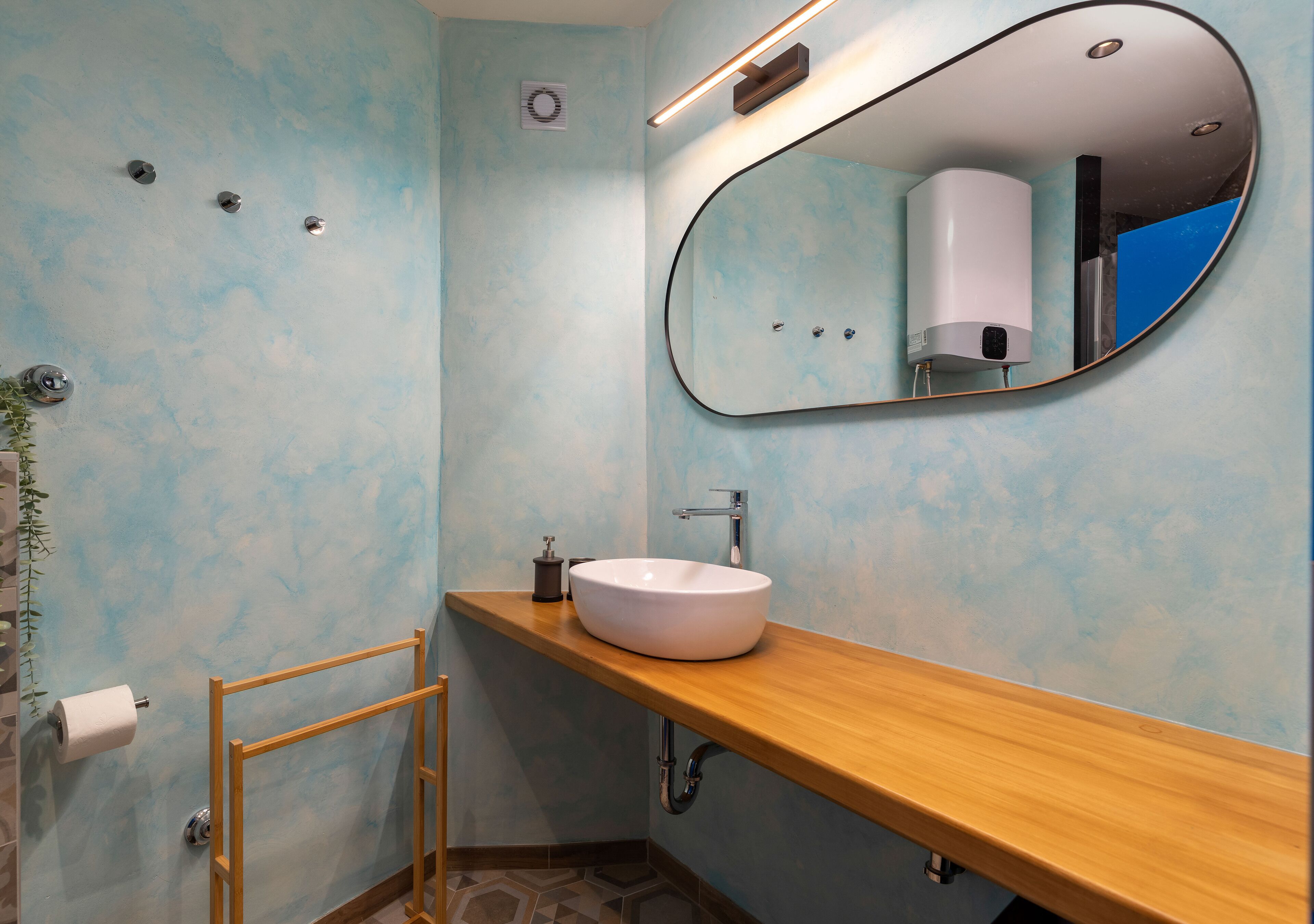 A bathroom with a wooden vanity, a white sink, a mirror, and a towel rack.