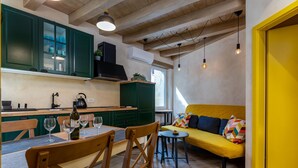 Uma cozinha compacta com armários verdes, uma mesa de jantar com cadeiras e um sofá amarelo numa sala luminosa com vigas de madeira.