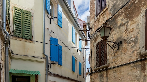 Uma rua de paralelepípedos estreita, ladeada por edifícios históricos com persianas tradicionais e um ar rústico.