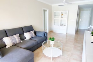 Ein Wohnzimmer mit grauem Sofa, einem Glastisch und einem weißen Schrank mit Glastüren.