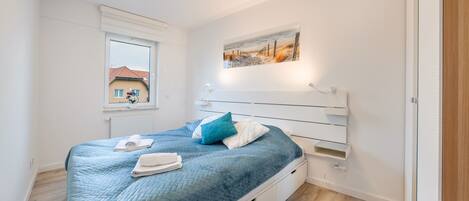 A bedroom with a bed, a window, a painting, and a radiator.
