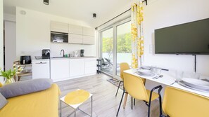 A modern kitchen with white cabinets, a built-in oven, and a dining area with yellow chairs and a white table. - Sun & Snow Platinum (Rewal)