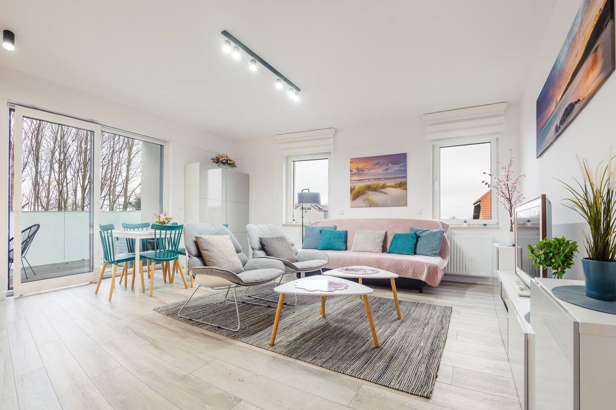 Ein modernes Wohnzimmer mit einer Couch, Sesseln, einem Couchtisch und einem Essbereich mit Tisch und Stühlen.